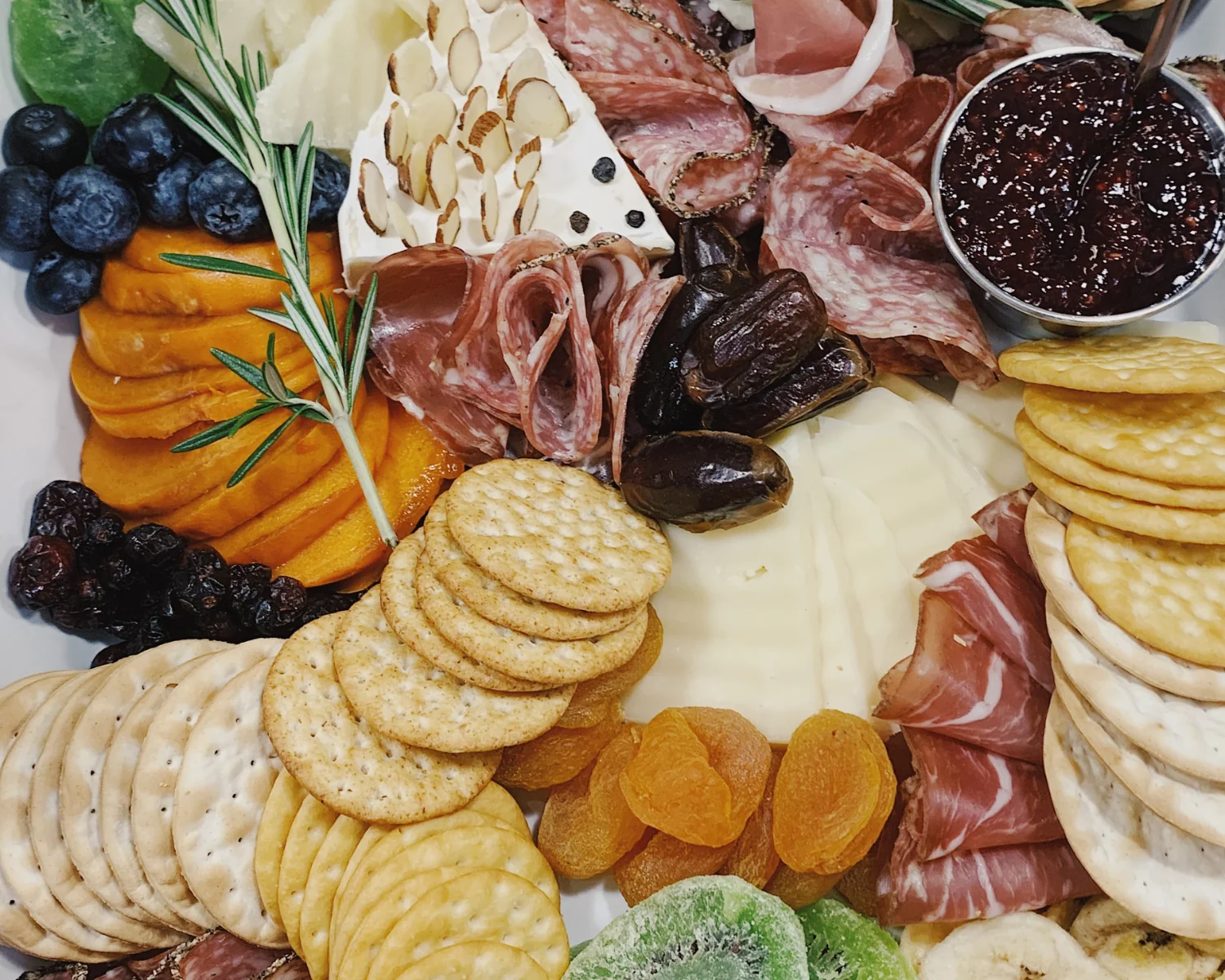 Charcuterie board of meats, cheese, crackers, nuts, fruit, and jam