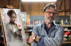 an artist next to one of his paintings of a girl