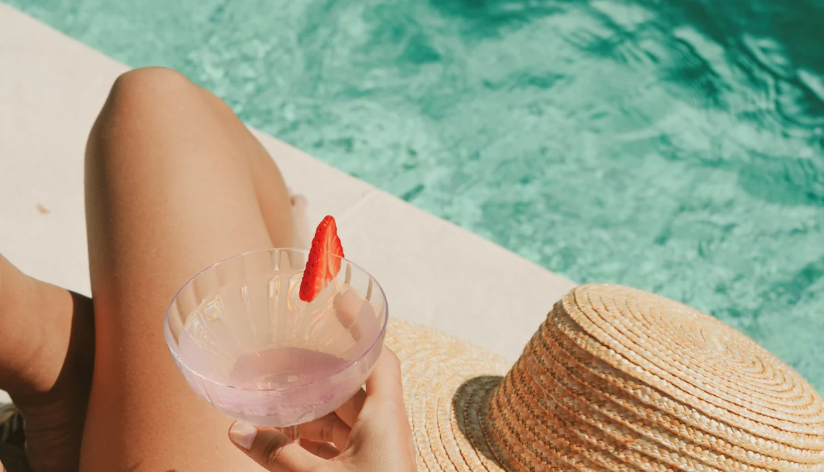 Person holding a drink by a pool